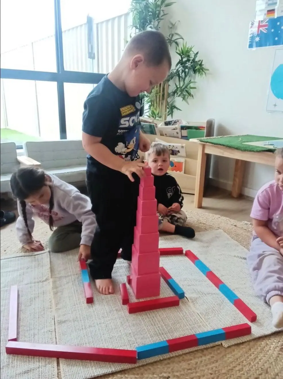 A toddler building a Montessori pink tower in a calm, plant-filled early learning classroom